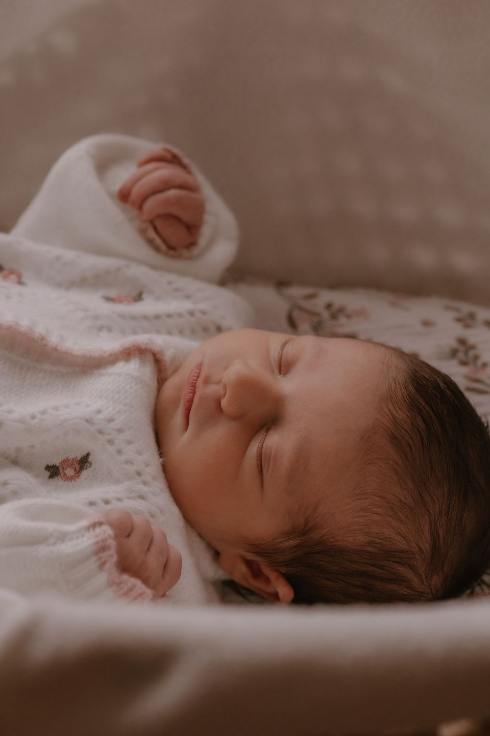 A sleeping newborn baby in white clothing rests peacefully on soft bedding.
