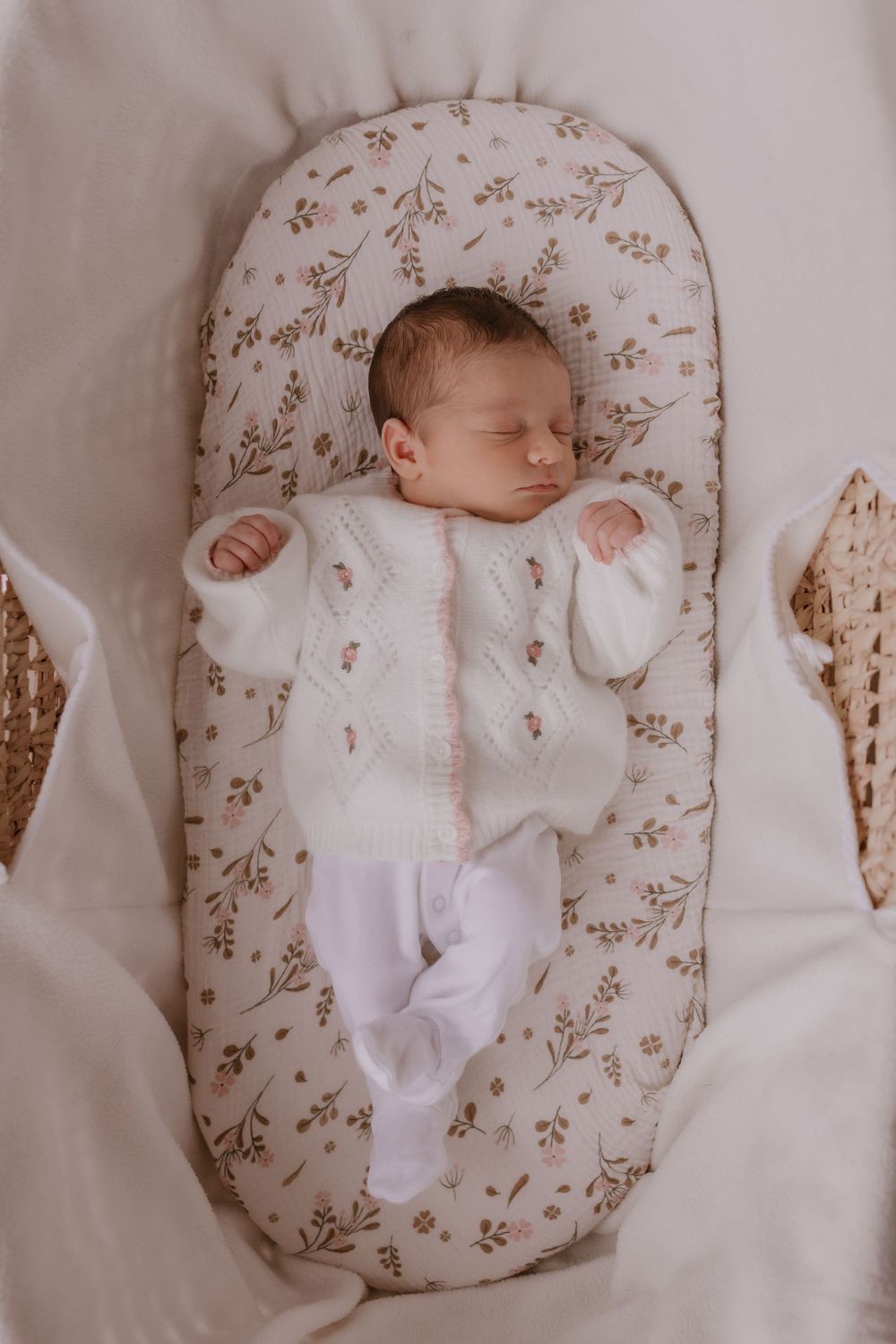 A sleeping newborn in white clothing rests on a floral-patterned lounger.