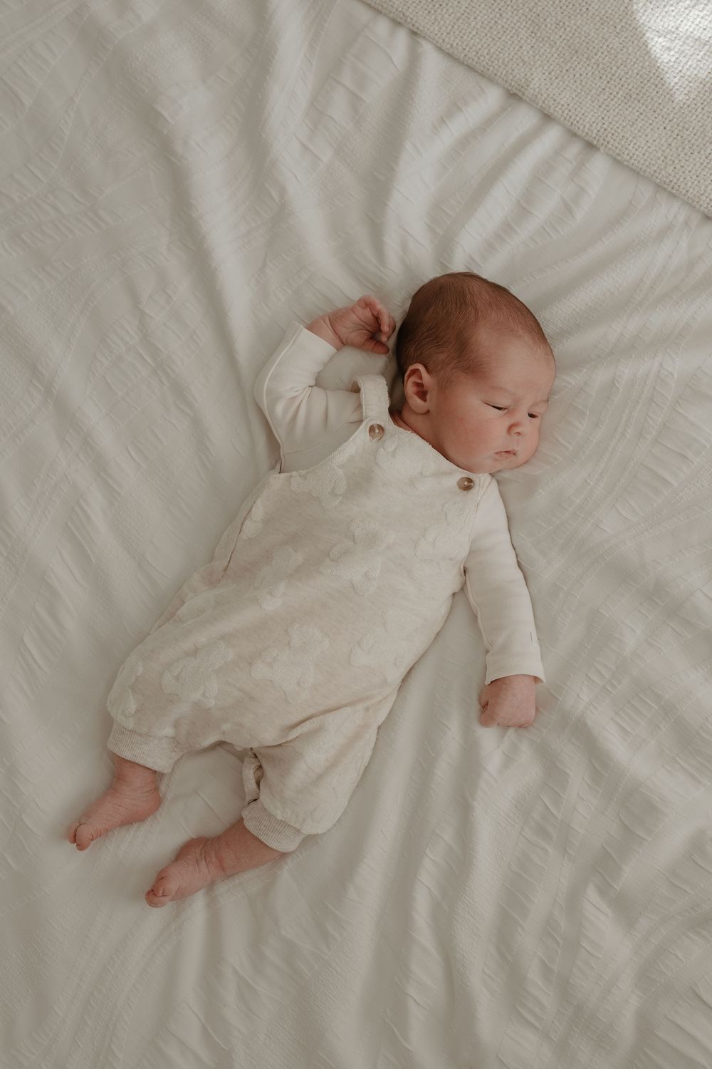 A sleeping baby in white clothing lies peacefully on crisp white bedding.