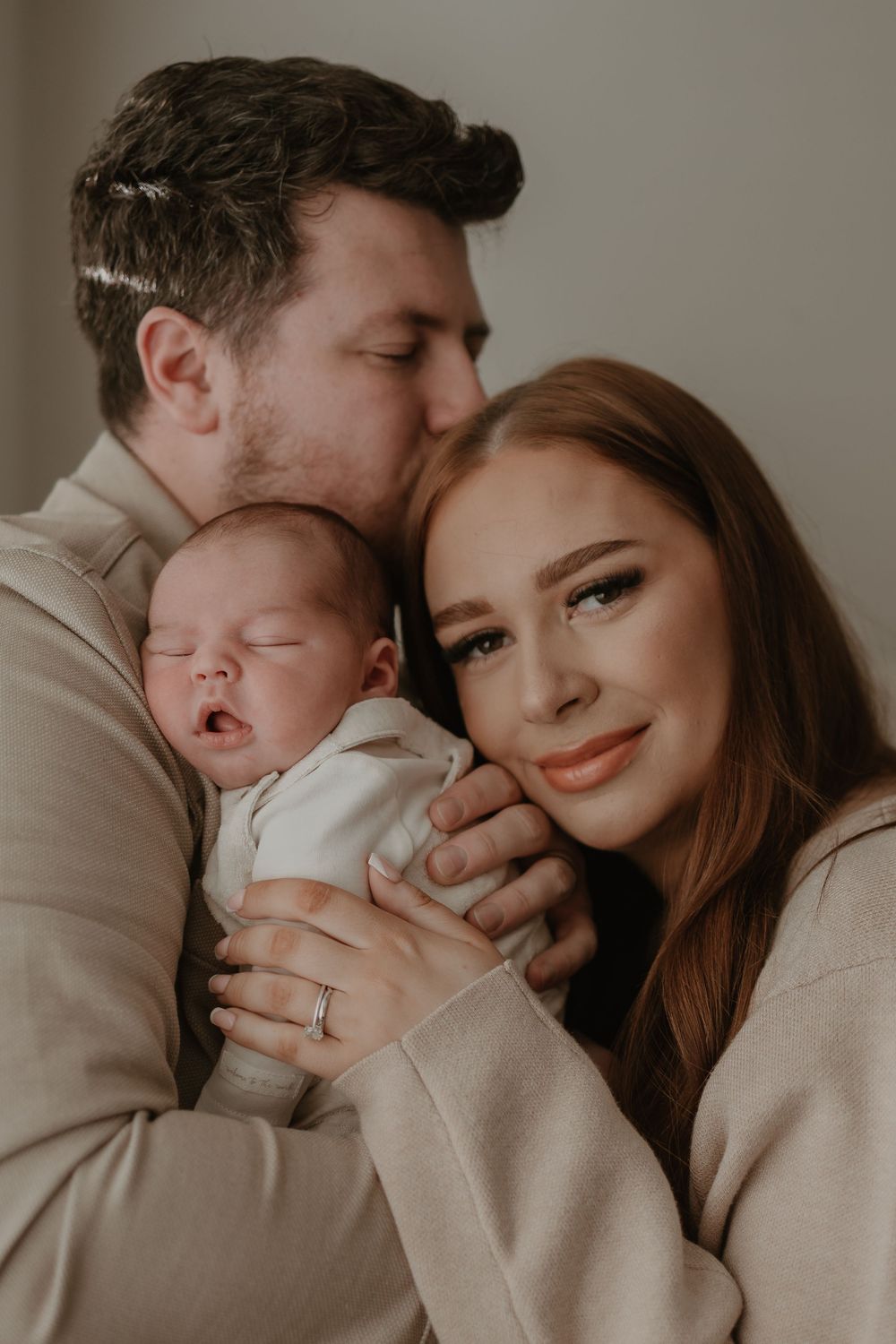 An intimate family moment with a newborn baby in neutral-toned clothing.