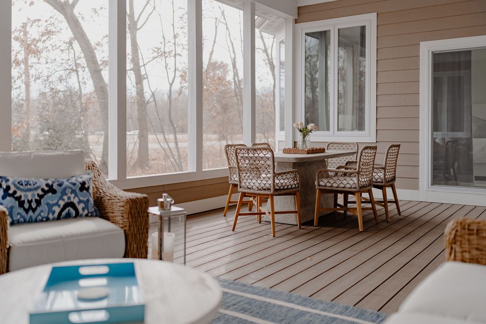 A modern sunroom with wood paneling features comfortable seating and large windows overlooking a wooded landscape.