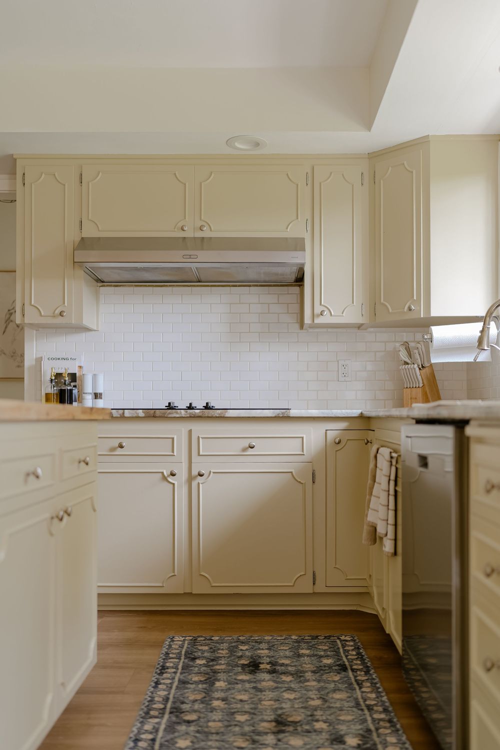 Cream colored kitchen cabinets with traditional panel details and white subway tile backsplash line the walls of this L-shaped space.