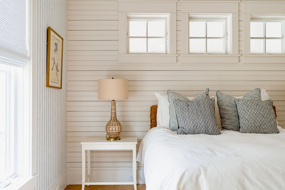 A bright white bedroom with shiplap walls features a modern bed, giraffe decor, and large windows letting in natural light.