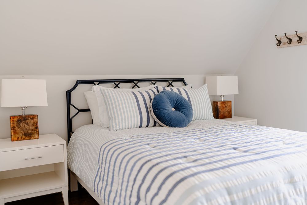 Cozy white and blue coastal bedroom with striped bedding, natural wood accents, and layered textiles.