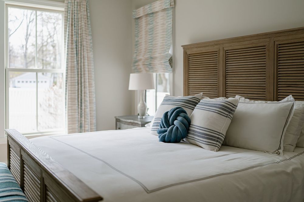A bright and airy bedroom with white bedding, wooden shutters, and natural light streaming through multiple windows.