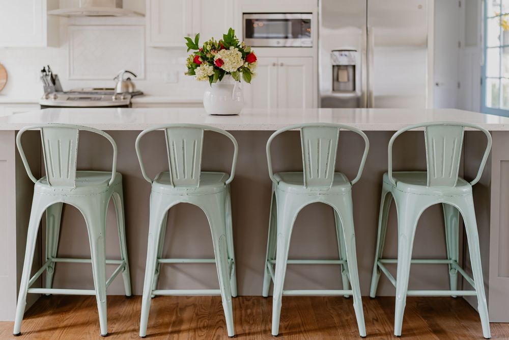A row of mint green metal dining chairs lines up against a white wall in a modern farmhouse kitchen setting.