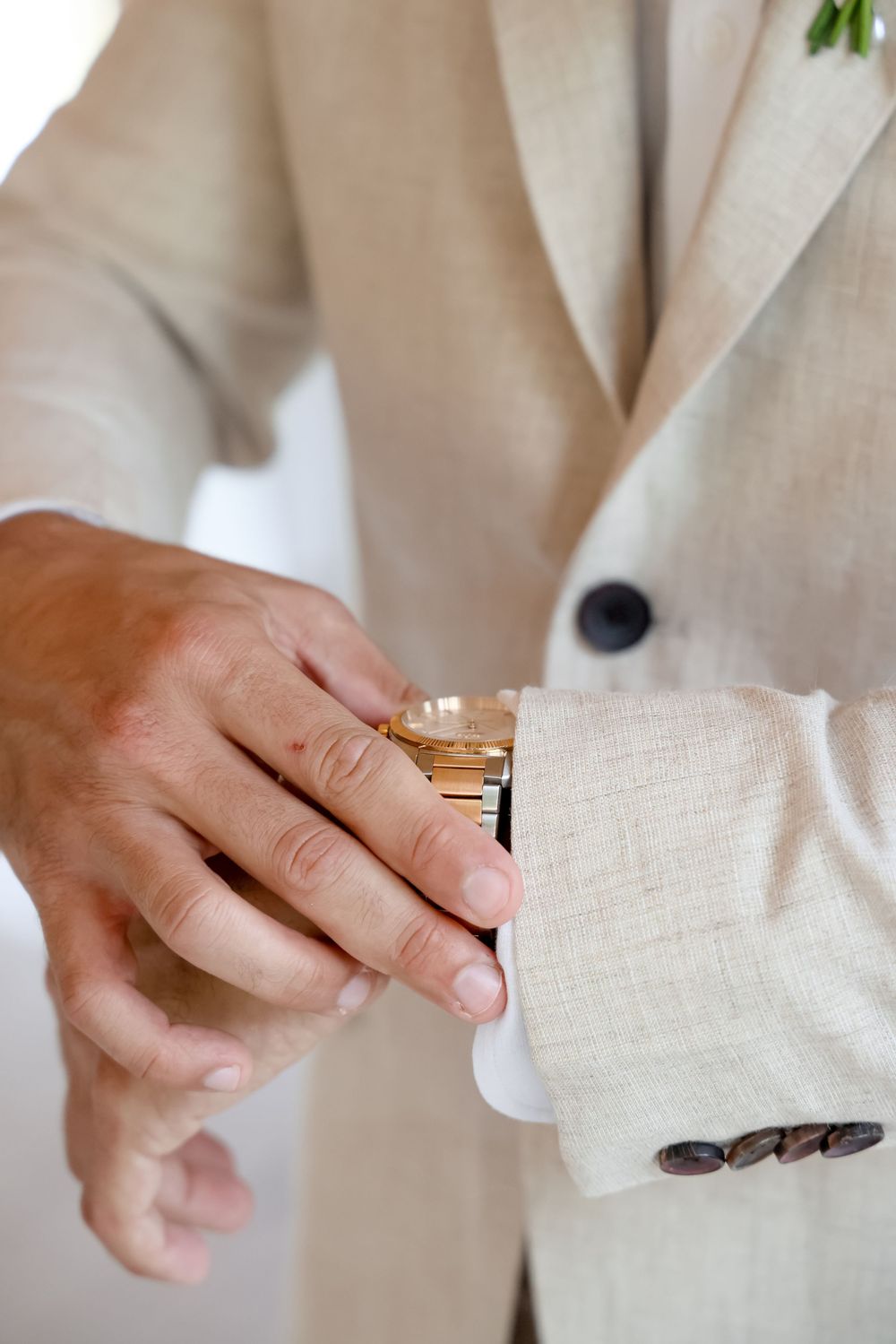 Sequence of hands fastening a button on a beige suit jacket sleeve.