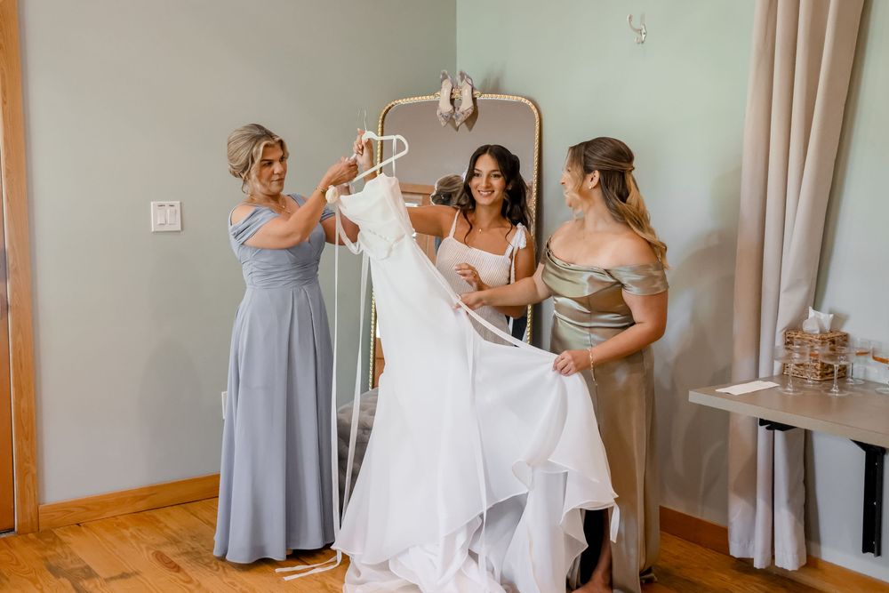 Bridesmaids in pale blue dresses help the bride prepare for her wedding day in a sunlit room.