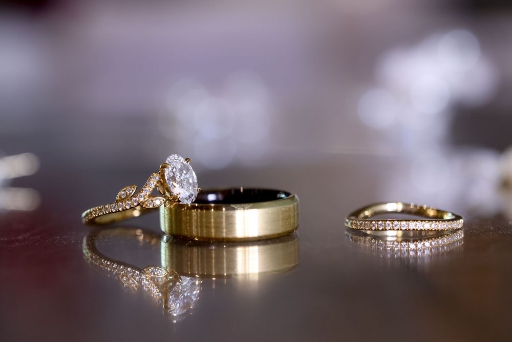 Three wedding rings with diamonds arranged on a reflective dark surface with soft lighting.