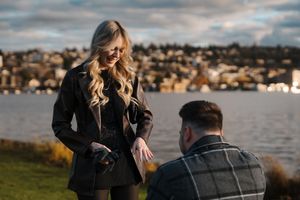 A couple sits together on a dock overlooking a scenic waterfront at sunset.