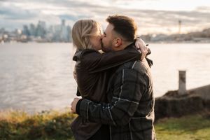 Two people share an intimate moment while embracing near a waterfront at sunset.