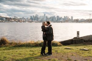 A couple shares a romantic moment overlooking Seattle's downtown skyline from a grassy waterfront viewpoint.