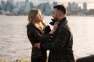 Couple sharing an intimate moment by the waterfront during golden hour with city skyline in background.