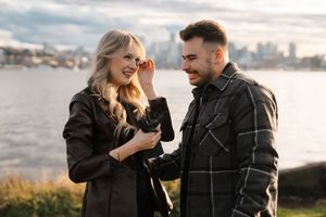 A couple shares a joyful moment together by the waterfront during golden hour with a cityscape in the background.