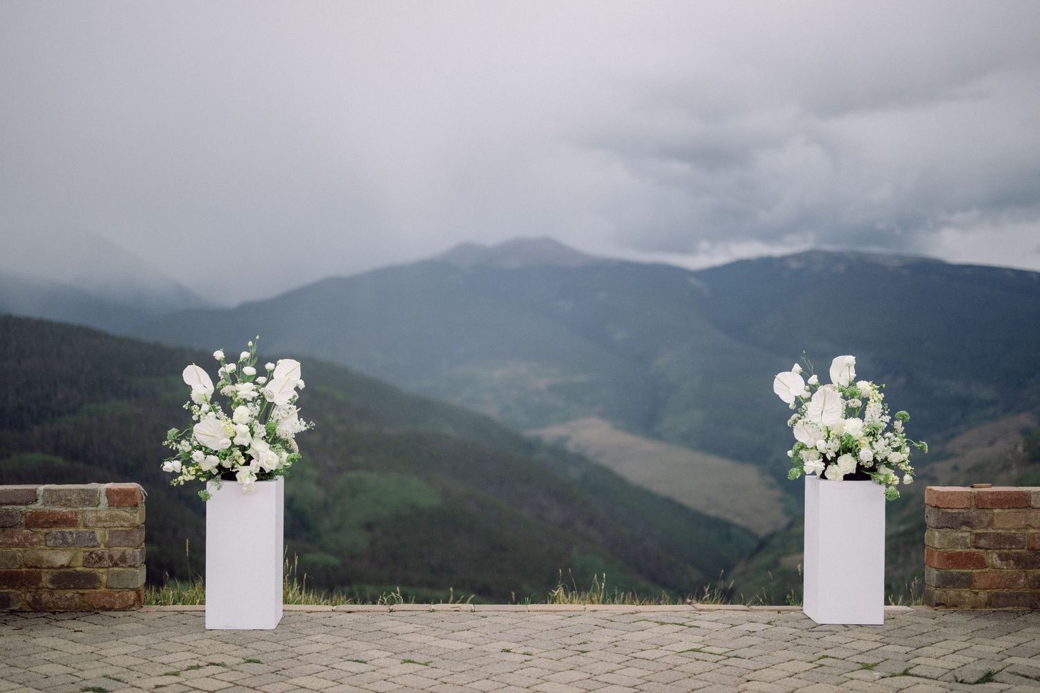 Misty mountain landscape with wooden railing and white decorative pillars against a cloudy sky.