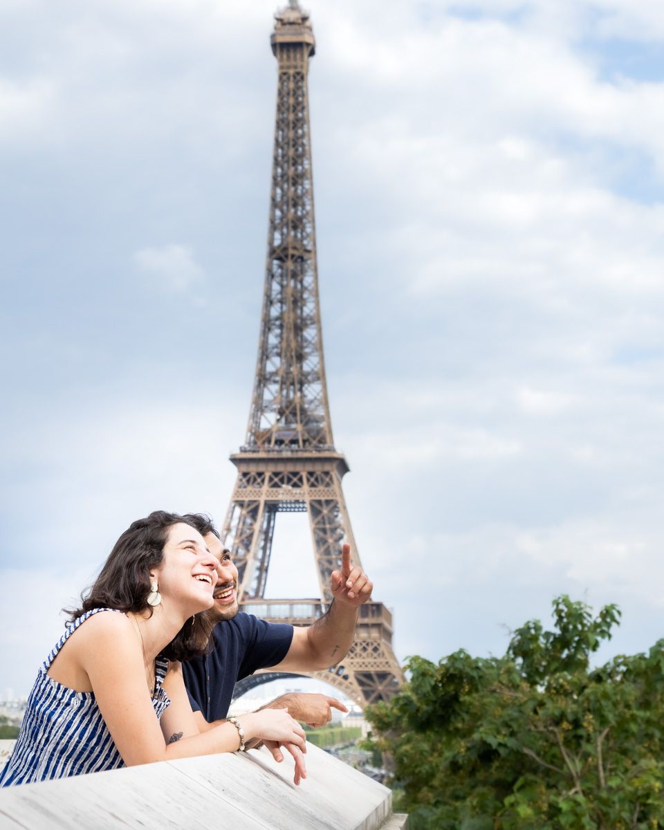 A couple shares a romantic moment near the iconic Eiffel Tower in Paris on a sunny day.