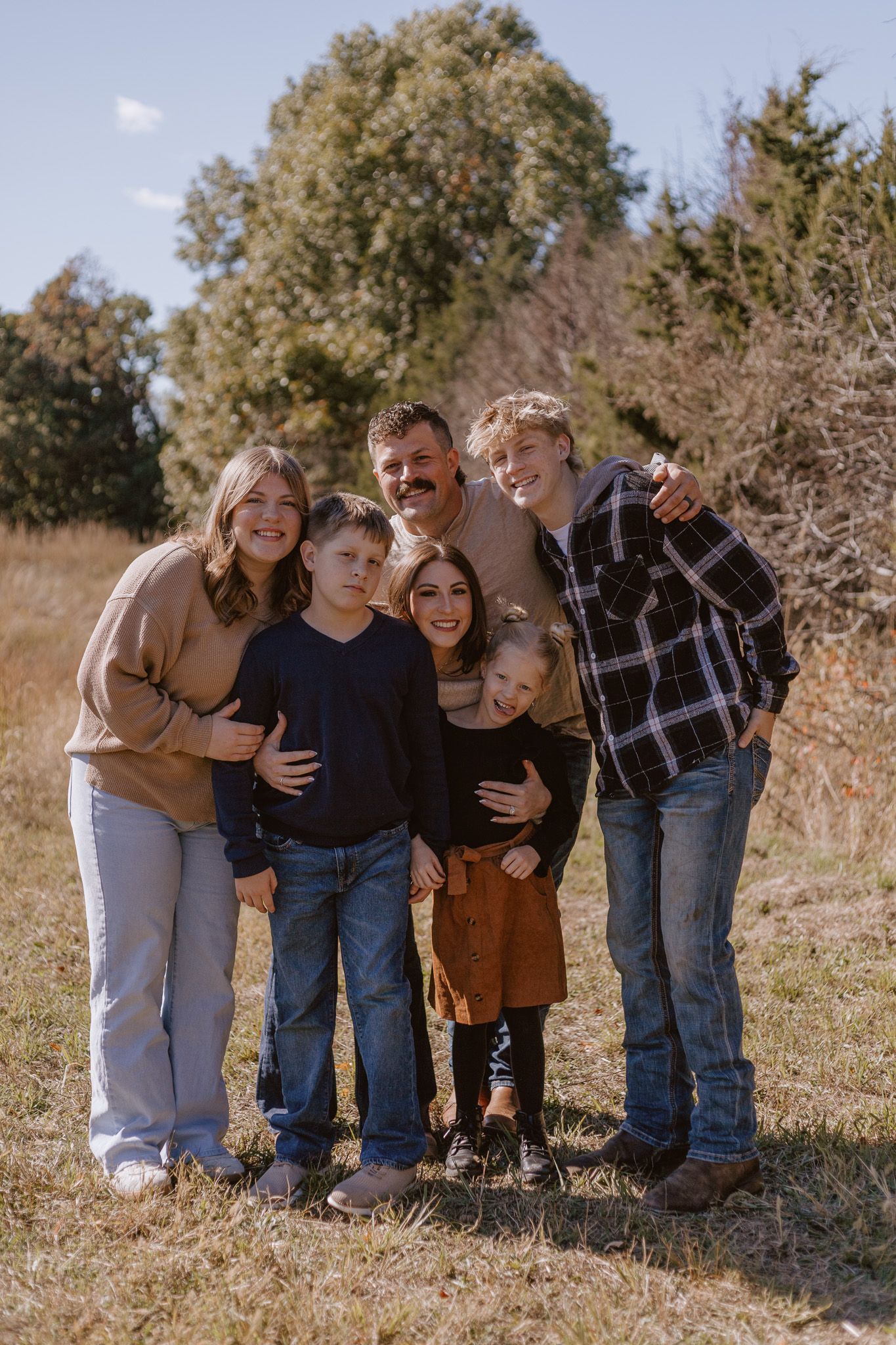 Happy family of six posing together in autumn field with trees and blue sky background.