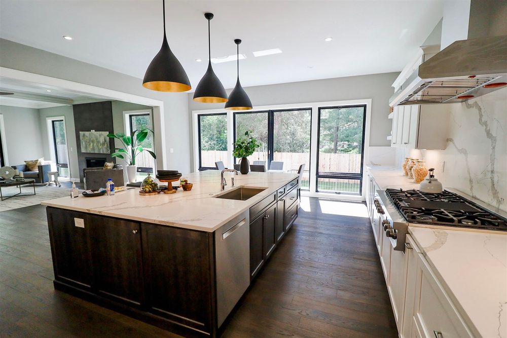Modern kitchen interior with pendant lights, white countertops and dark wood flooring.
