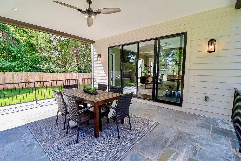 Spacious covered outdoor patio with concrete flooring and ceiling fan overlooking a green landscape.