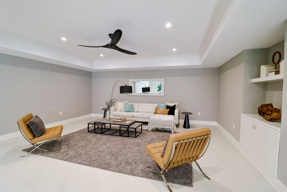 Large basement recreation room with grey carpet, ceiling fan, and modern yellow accent furniture.