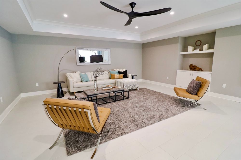 Open basement living area with recessed lighting, grey walls and wooden accent chairs.