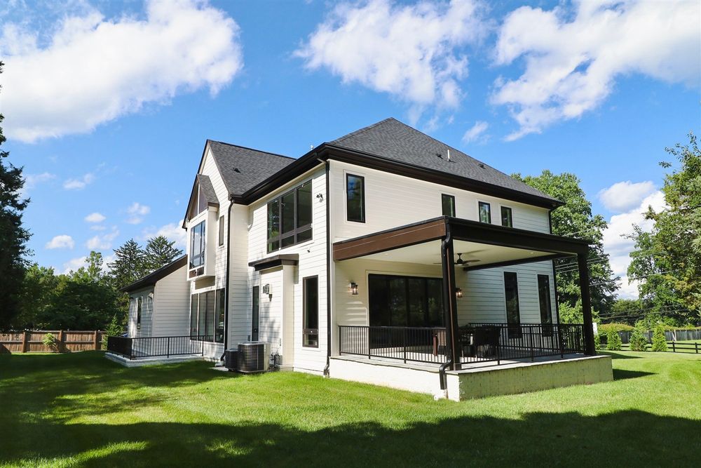Modern white and black two-story house with covered patio and manicured lawn under blue sky.