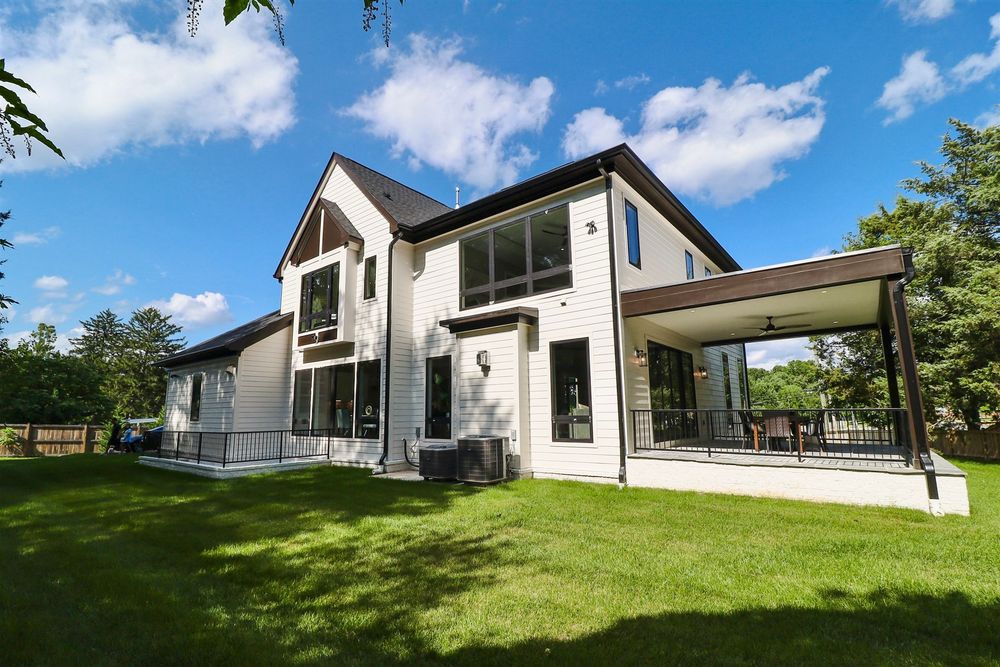 Contemporary white house exterior with large windows and covered porch surrounded by green lawn.