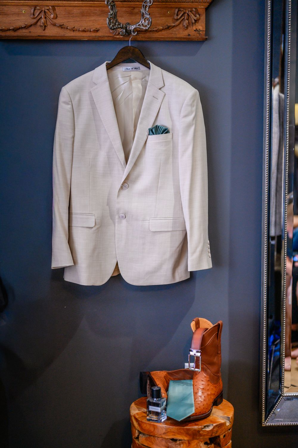 White wedding suits and brown leather shoes displayed against a dark blue wall for preparation.
