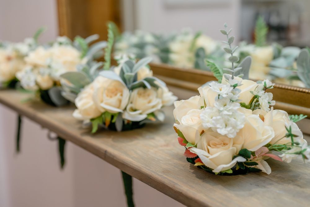 Delicate peach roses and dusty blue eucalyptus leaves arranged as wedding boutonnieres on a wooden surface.