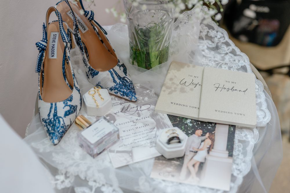 Light blue bridal shoes with crystal details displayed among wedding stationery and lace.