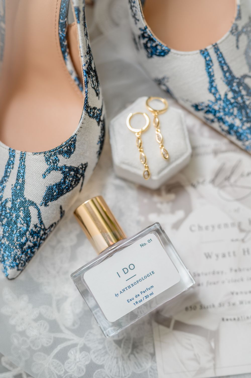 Wedding details including perfume bottles labeled 'I DO' and delicate blue and gold accessories on marble.