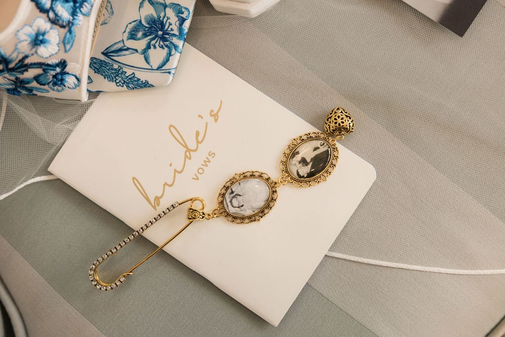 Gold drop earrings with pearl details lay elegantly on a white paper with blue floral decorative elements.
