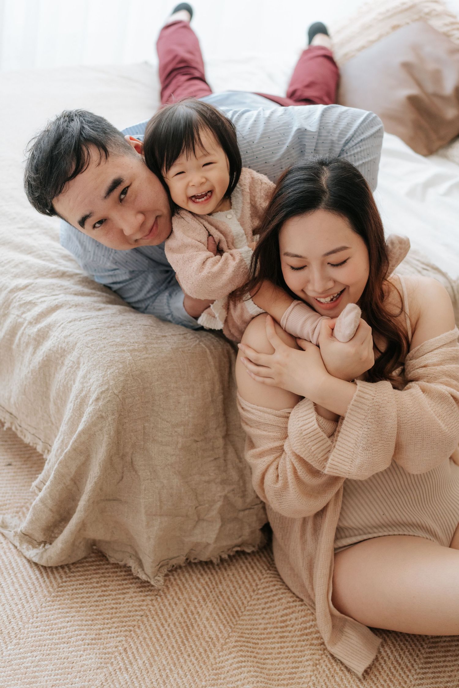A family shares joyful moments together while relaxing on a cozy bed with neutral-toned bedding.