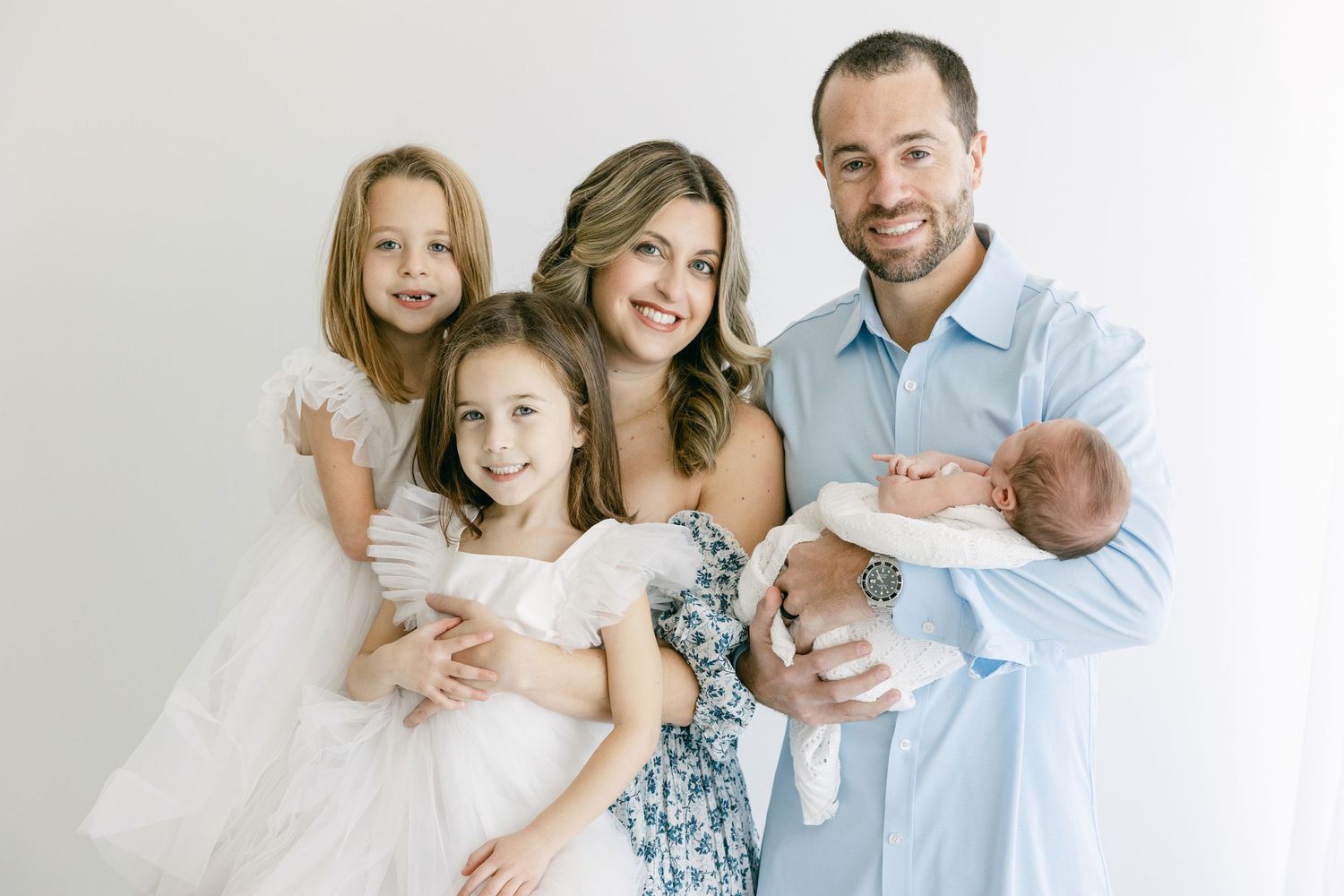 A family of five wearing white and blue poses together against a light background for a portrait.