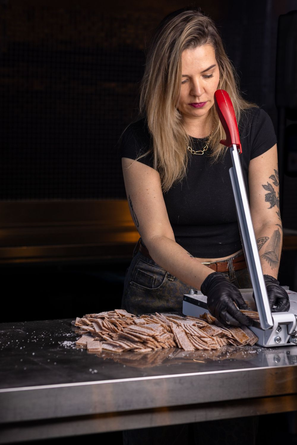 A chef in black gloves uses a vacuum sealer to preserve sliced meat on a dark countertop.