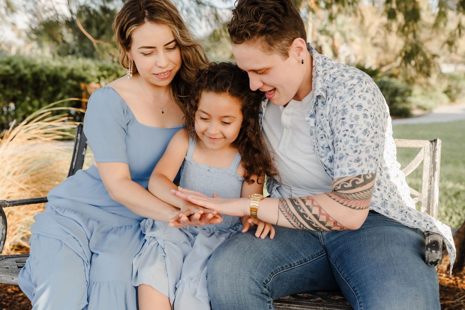 A family wearing coordinating blue outfits sits together outdoors sharing a tender moment in natural lighting.