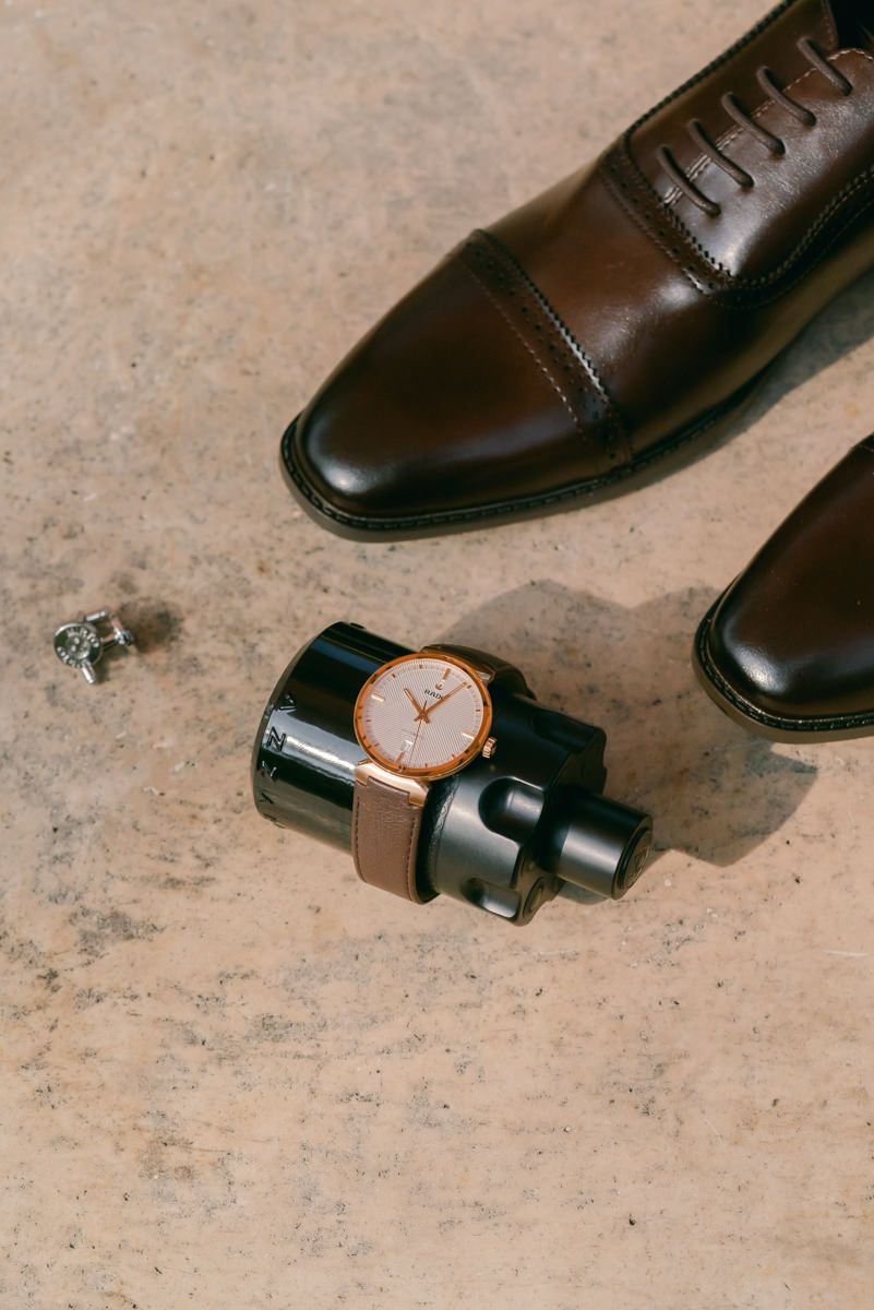 A sequence of brown leather dress shoes arranged diagonally with a wristwatch creating a minimalist composition.