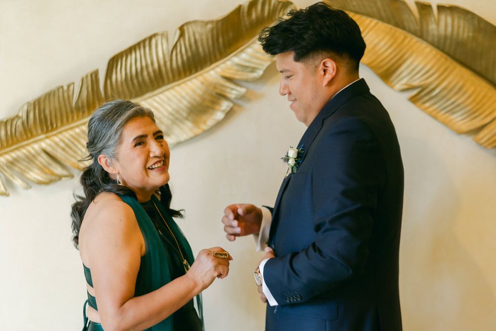 Two people share a joyful moment while exchanging rings during an intimate wedding ceremony under gold decor.