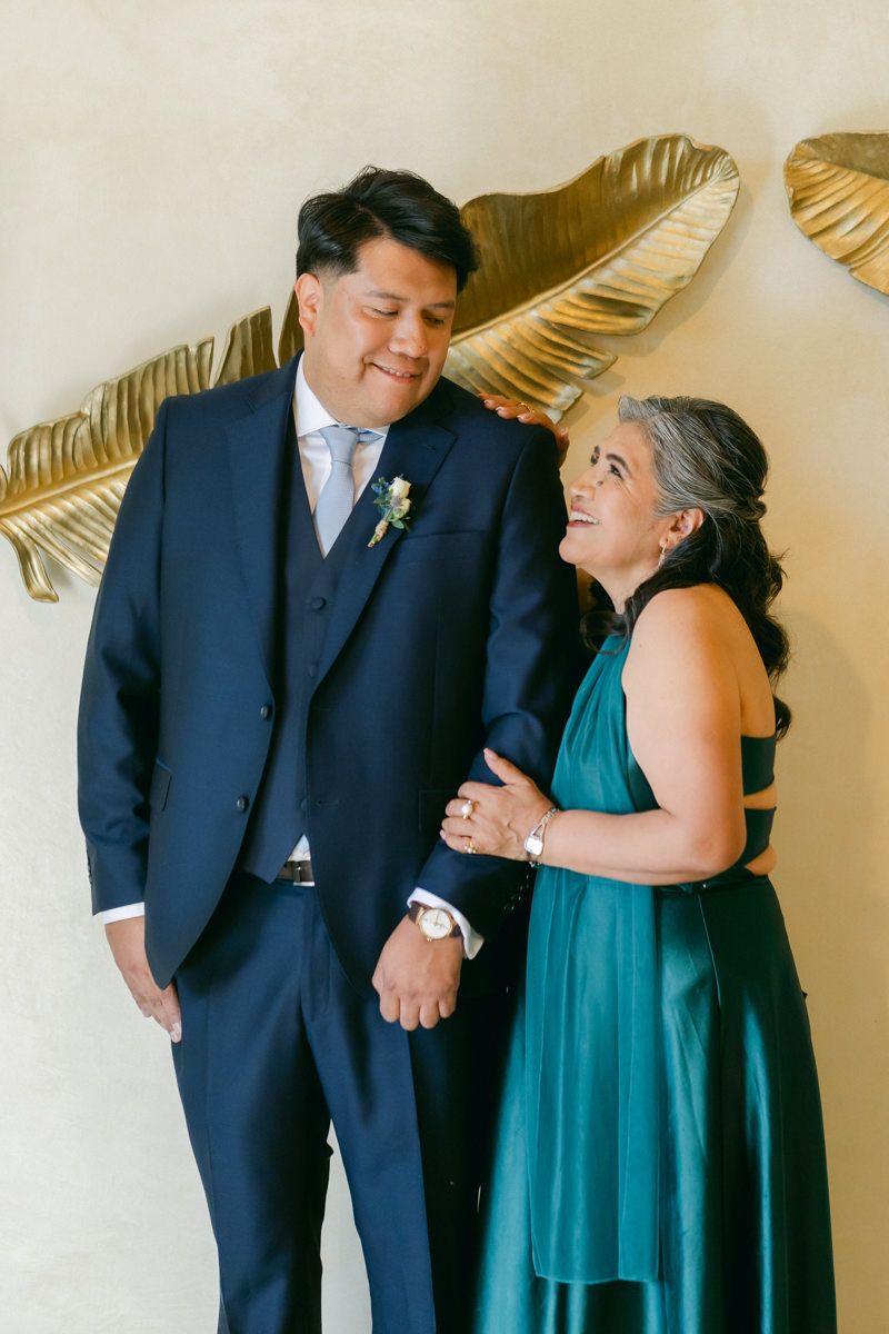 Wedding couple in navy suit and teal dress share a joyful moment against gold decor.