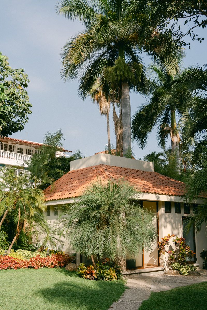 Tropical landscaping with palm trees and terra cotta roofed buildings along a winding pathway in a lush garden setting.