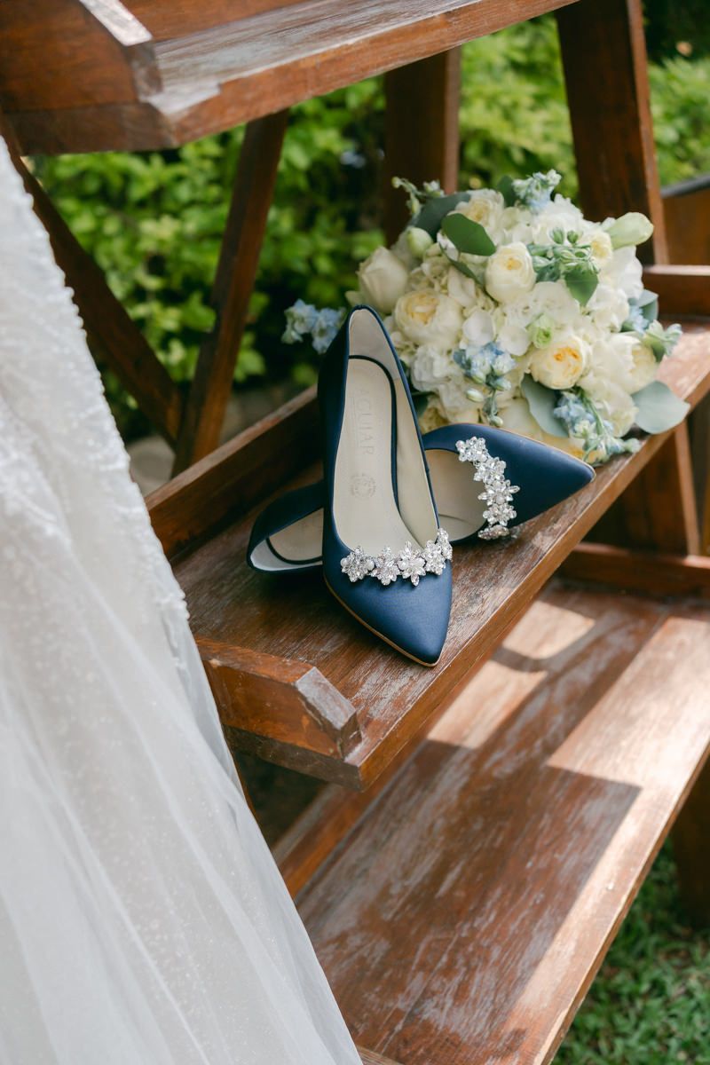 Navy blue bridal shoes with lace details sit next to a white and blue floral bouquet on wooden stairs.