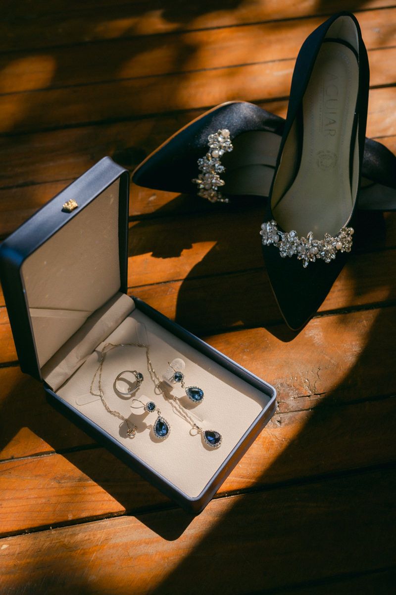Wedding jewelry and accessories including sapphire necklace, earrings, and crystal headpiece displayed on wooden surface.