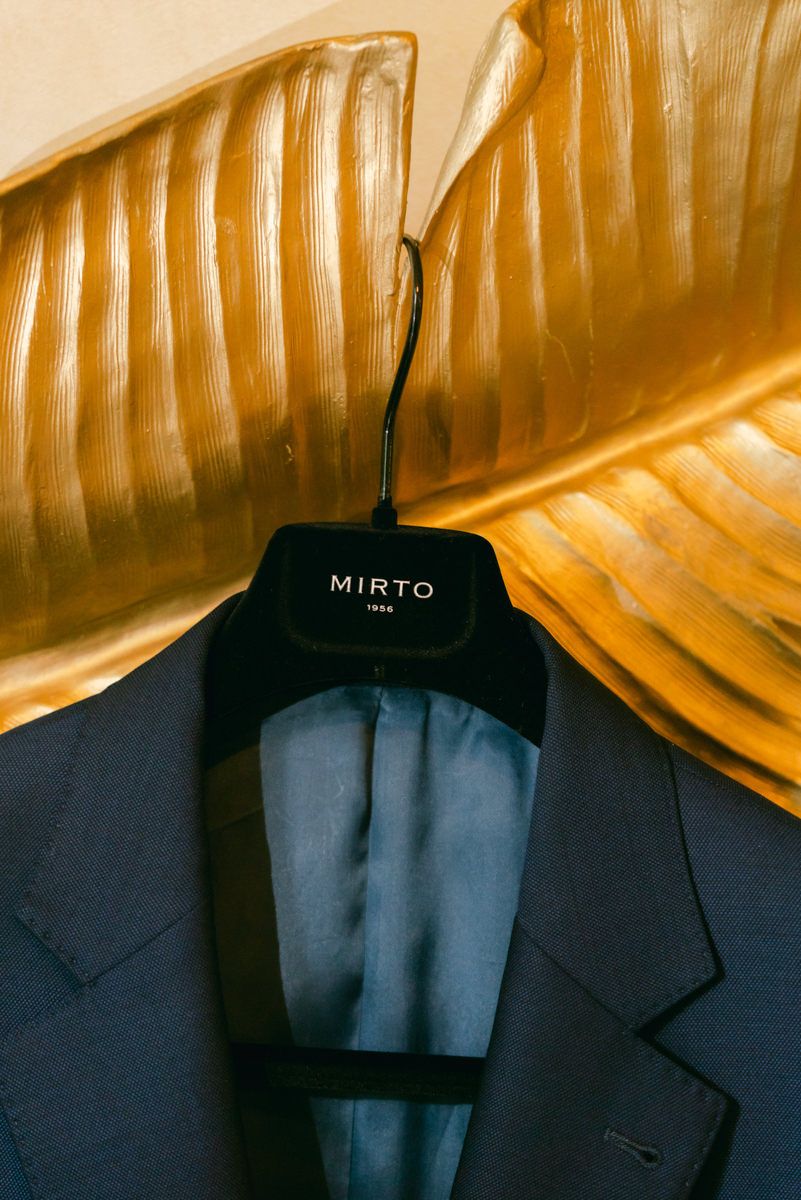 Dark suit jackets hanging on black hangers against a golden-toned textured wall.