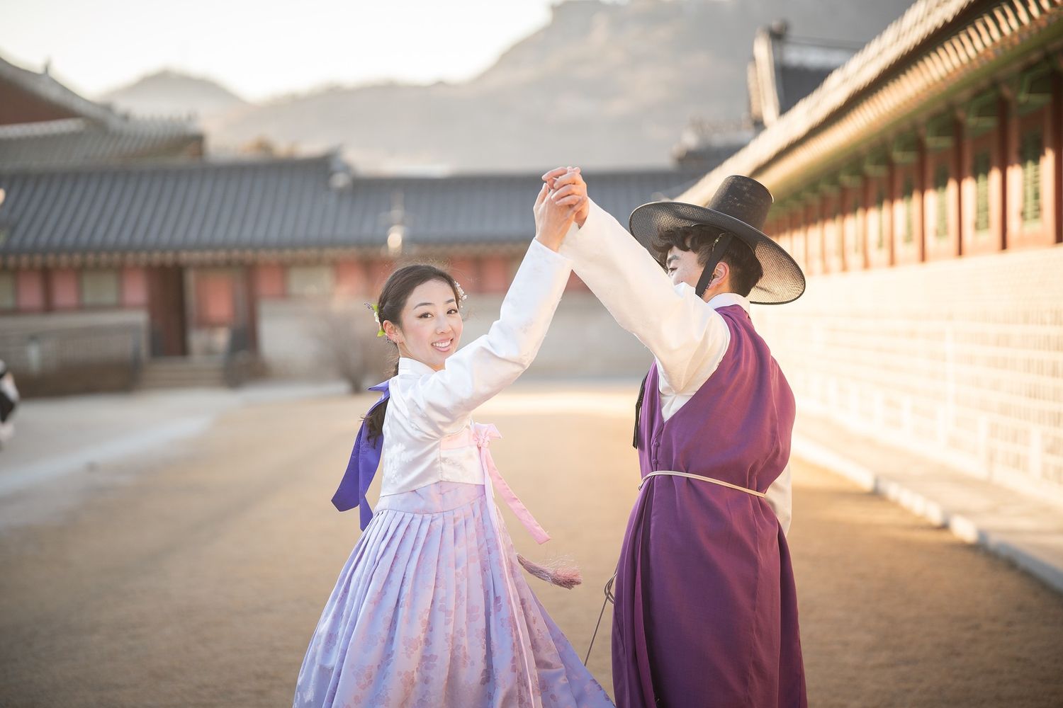 Two people in traditional Korean hanbok dresses walk together along a temple courtyard at sunset.