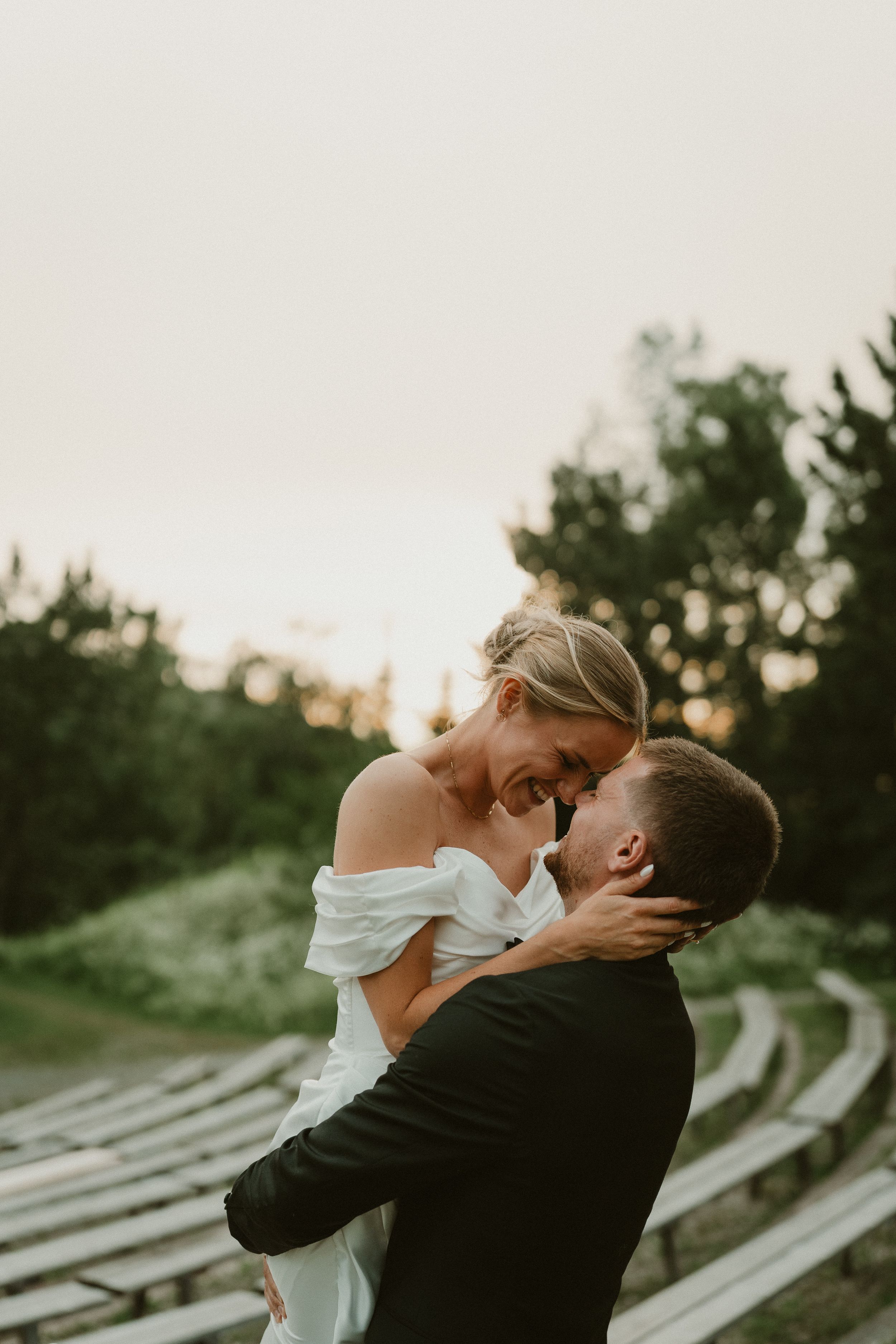 A wedding couple shares a romantic moment on a paved walkway surrounded by guests and greenery.