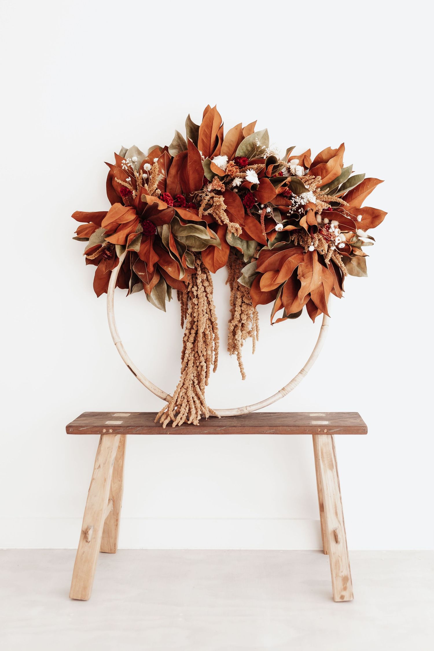 Rustic dried flower arrangement in rust tones displayed on wooden bench.