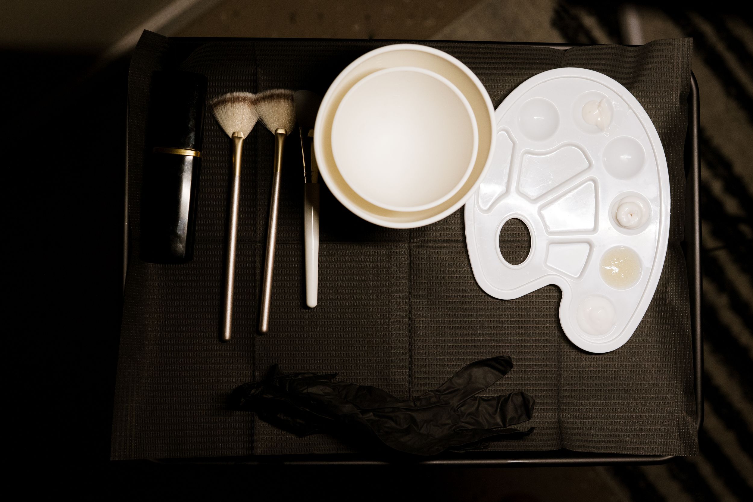 Art supplies including paint brushes, a palette, and white ceramic plates arranged on a dark surface.