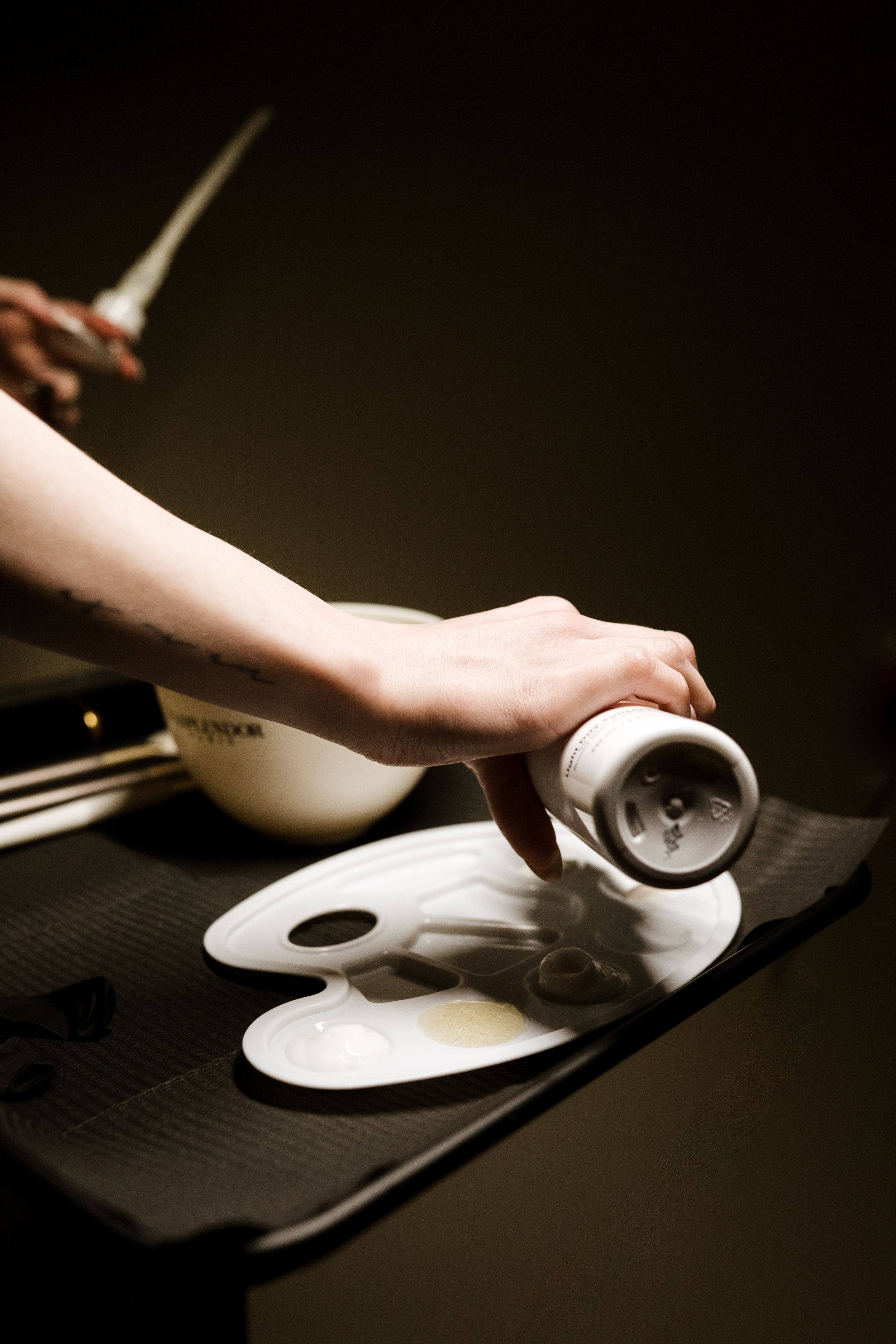 Hands carefully applying white porcelain mask to face in dramatic lighting sequence.