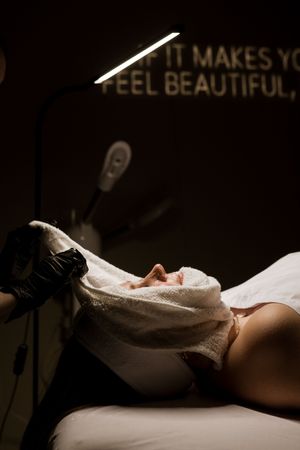 A person lies on a bed in dark lighting with soft shadows creating a moody, intimate atmosphere.
