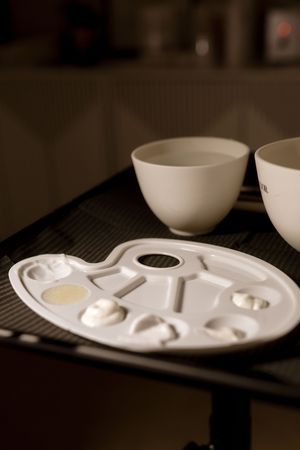 A series of white ceramic bowls and plates arranged on a dark surface in a minimalist style.